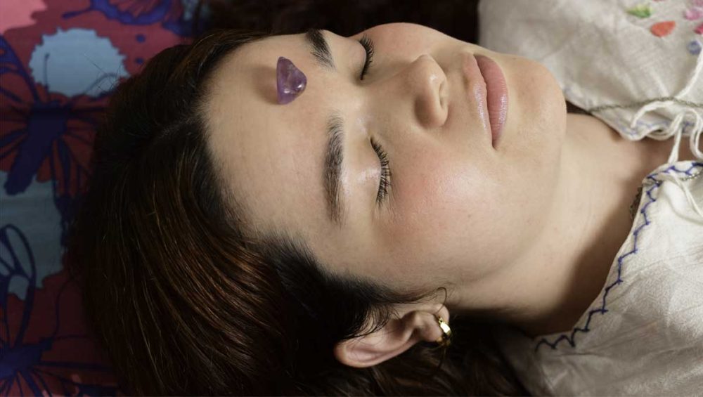 person lying with an amethyst crystal placed on the crown chakra during meditation