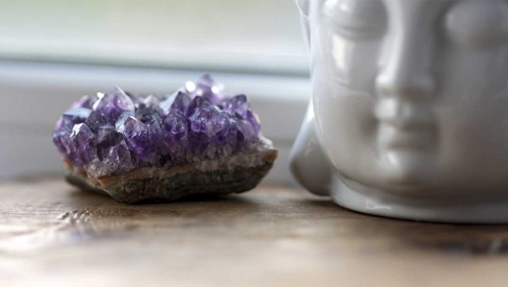 Amethyst crystal cluster beside a meditation statue symbolizing calm awareness and intuitive reflection