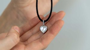 Heart-shaped memorial necklace designed to hold dog ashes resting in a person’s hand