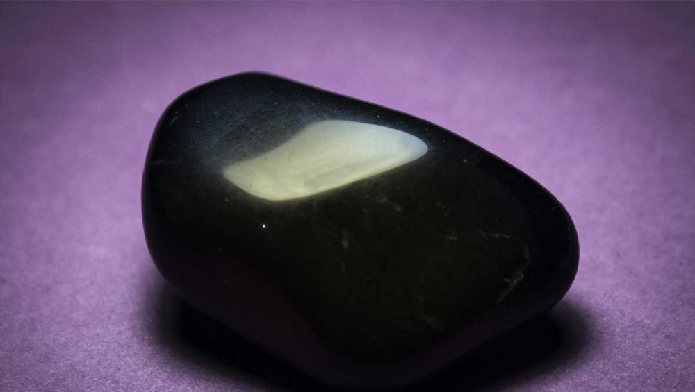 polished black onyx stone resting on a purple surface