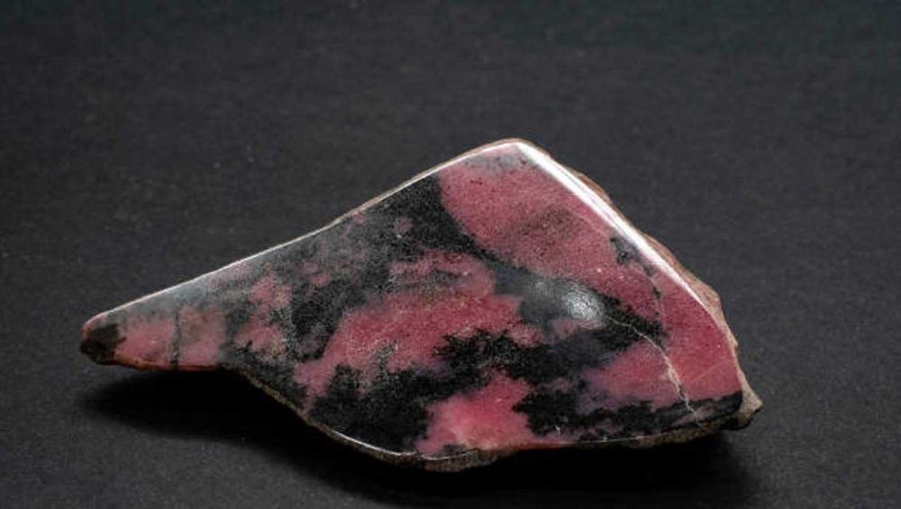Polished rhodonite stone with pink tones and black veining on a dark background