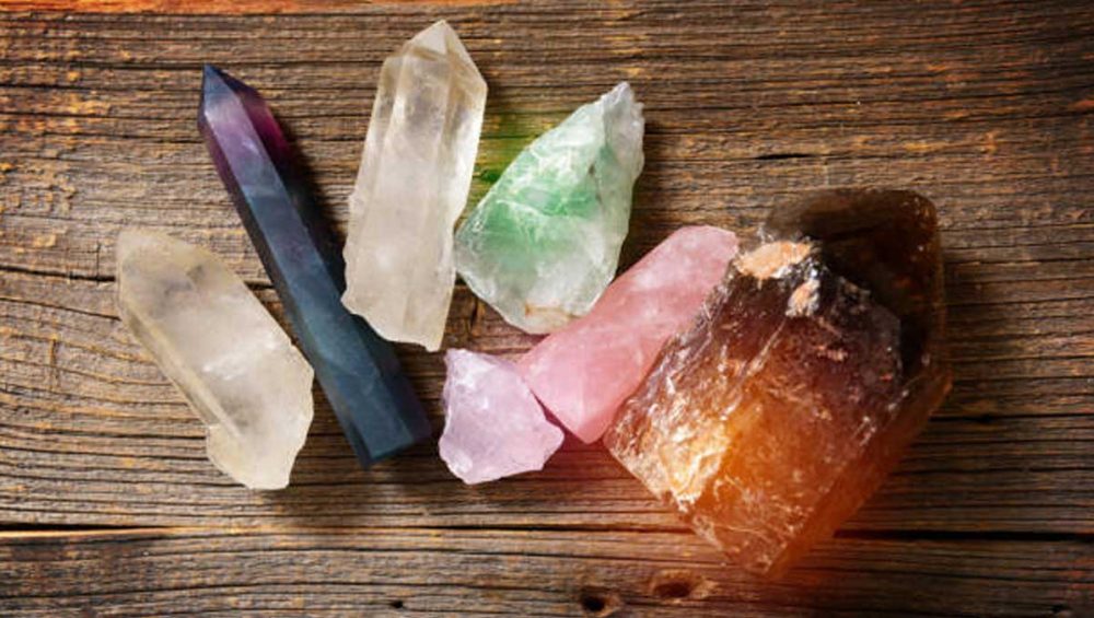 A variety of different crystals including clear quartz, rose quartz, green fluorite, and smoky quartz arranged on a rustic wooden surface