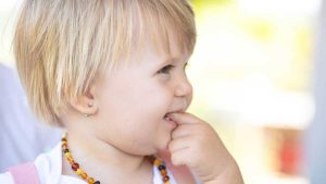 baby wearing amber teething necklace while gently chewing fingers