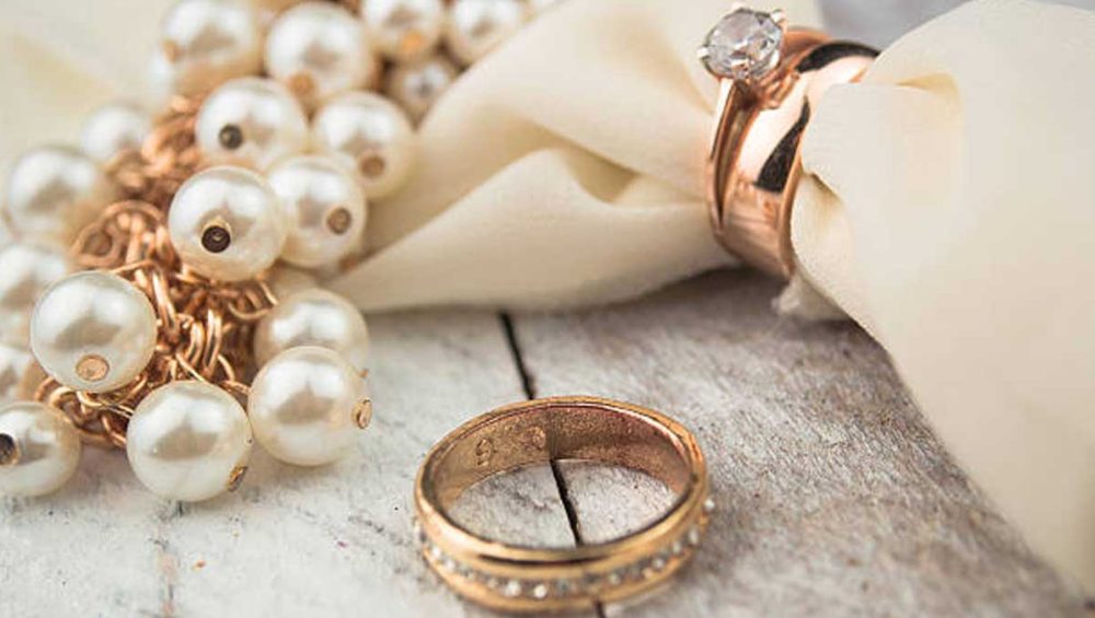 gold wedding rings and pearl jewelry on a rustic surface
