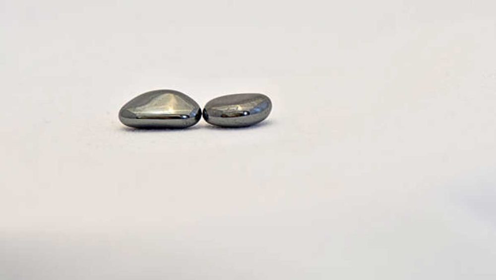 two polished hematite stones with a reflective metallic surface on a light background