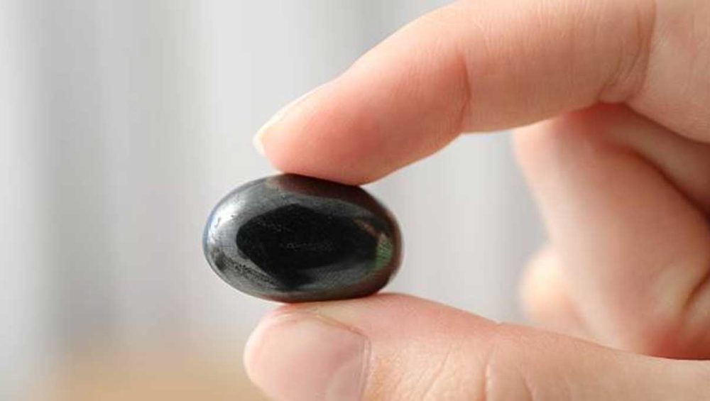 person holding a smooth dark hematite stone between fingers