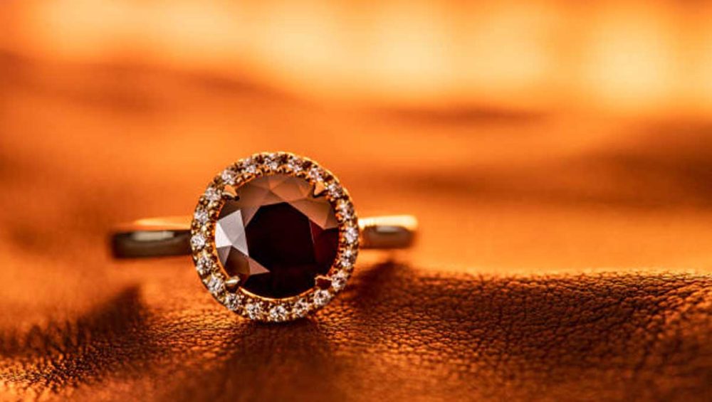 gold ring with deep red gemstone on a warm orange background
