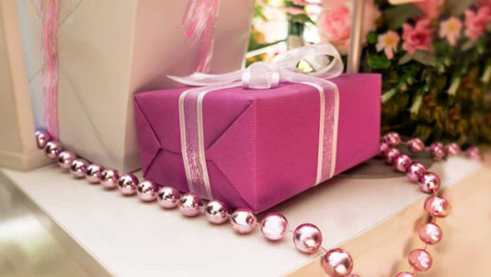 pink wrapped gift box with ribbon and beaded necklace displayed on a table