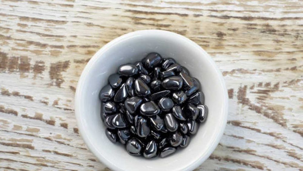 polished hematite stones in a white bowl on a wooden surface