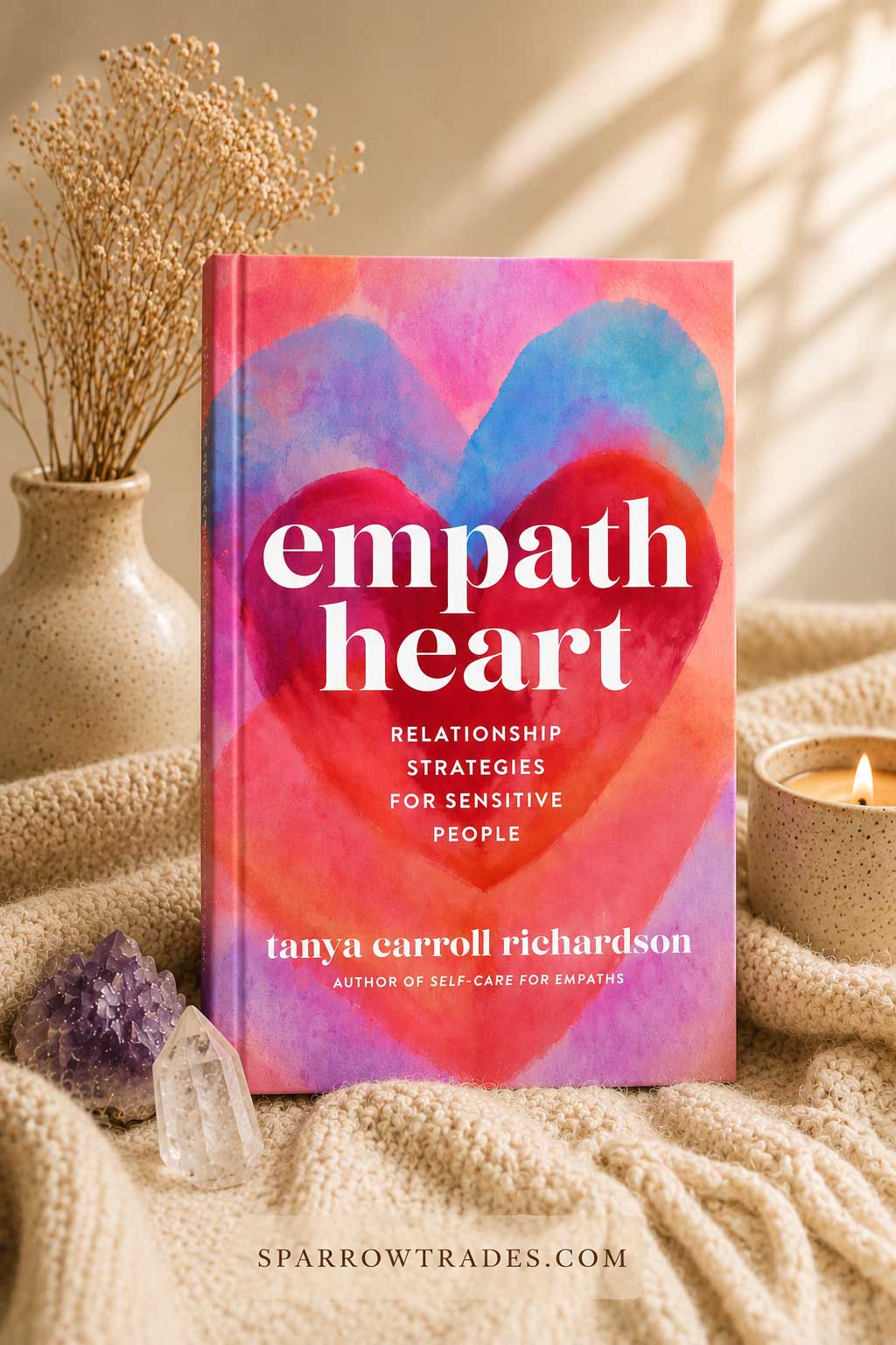 Cozy styled image of the book Empath Heart by Tanya Carroll Richardson surrounded by soft blankets, crystals, candles, and dried flowers.