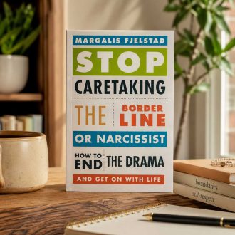 Book cover of Stop Caretaking the Borderline or Narcissist displayed upright on a wooden table in a warm indoor setting with books, a notebook, and natural light.