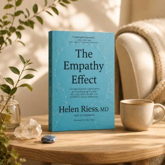 The Empathy Effect book displayed on a wooden table beside a ceramic mug, greenery, and decorative stones in a softly lit room.