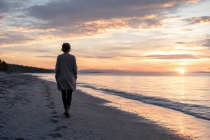 Woman walking alone along a quiet shoreline at sunset
